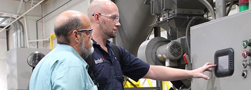 Two Men Looking At A Metal Scrap Conveyor Panel